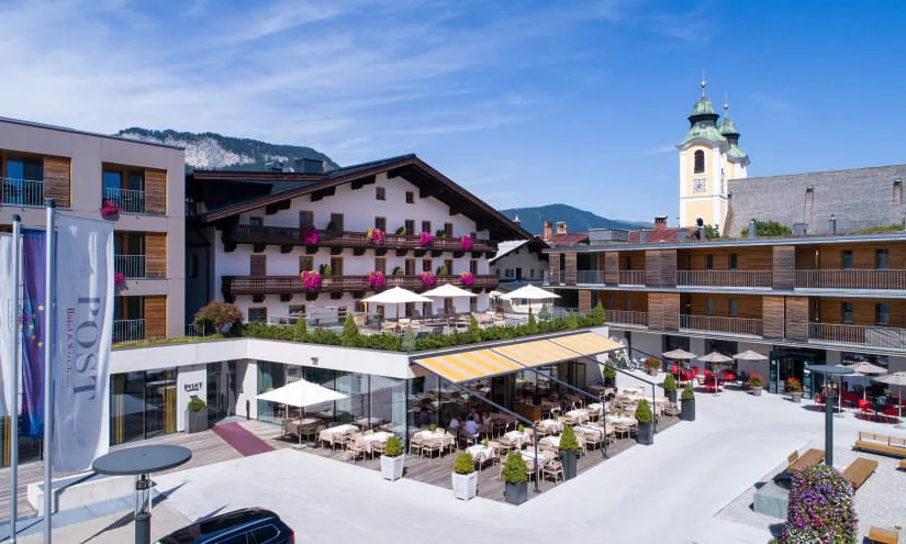 Panoramablick auf ein Hotel mit Restaurantterrasse und umliegenden Bergen.