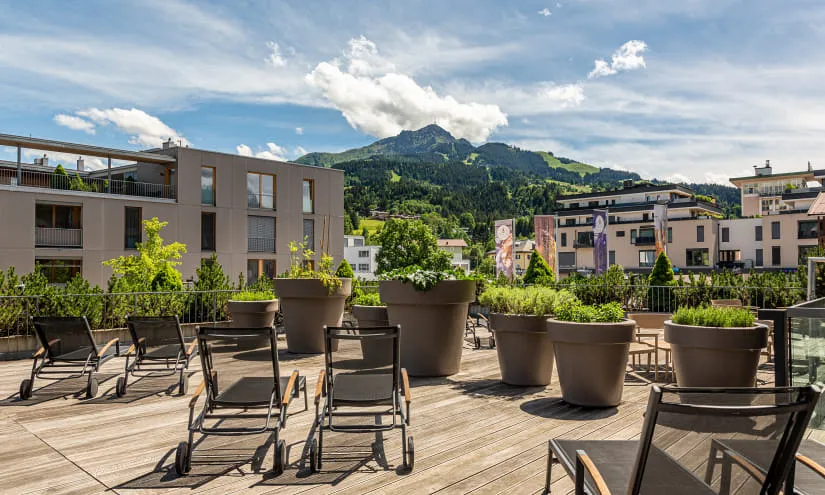 Terrasse mit Liegen und Pflanzen, Blick auf Berge und moderne Gebäude.