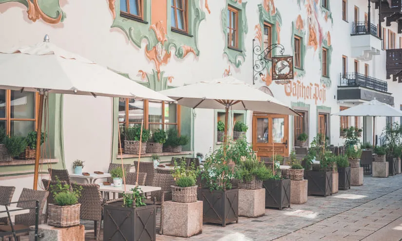 Terrasse mit Tischen und Pflanzen vor einer dekorierten Wand.