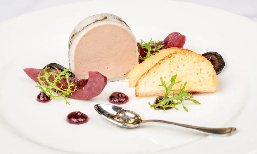 Gourmetgericht mit Fleischpastete, Brot und Beerenkompott auf weißem Teller.