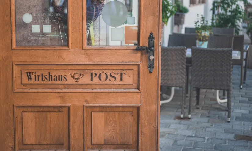 Holztür mit der Aufschrift 'Wirtshaus POST' und Sicht auf Außenbereich