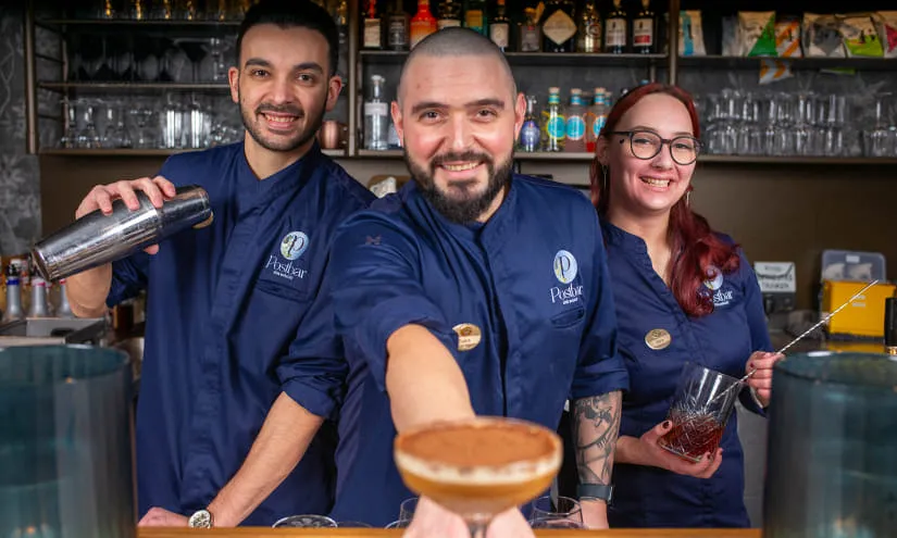 Drei Barkeeper stehen hinter einer Bar mit Getränken.