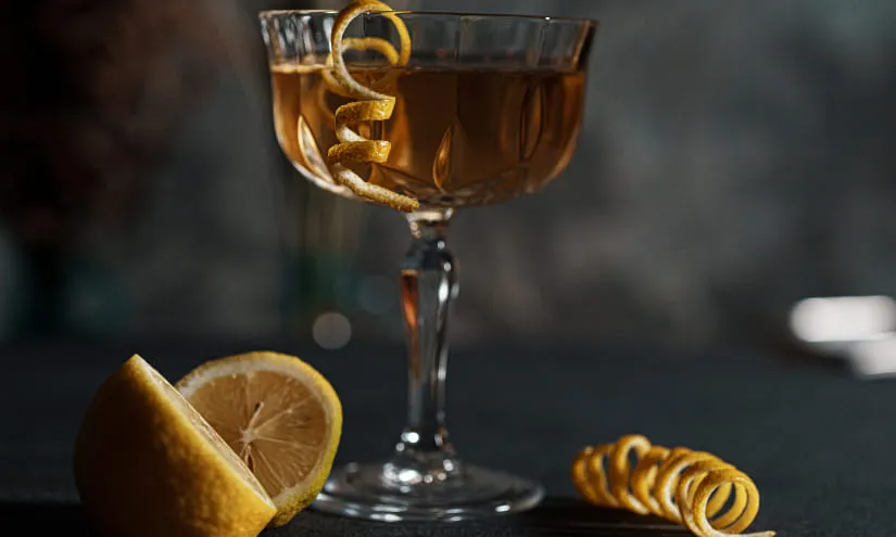 Cocktail in einem Glas mit Zitronenzesten und -scheibe auf dunkler Fläche