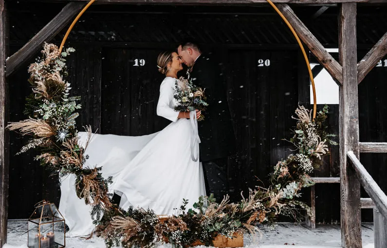 Paar in Winterhochzeit, umgeben von einem Kranz aus Pflanzen.
