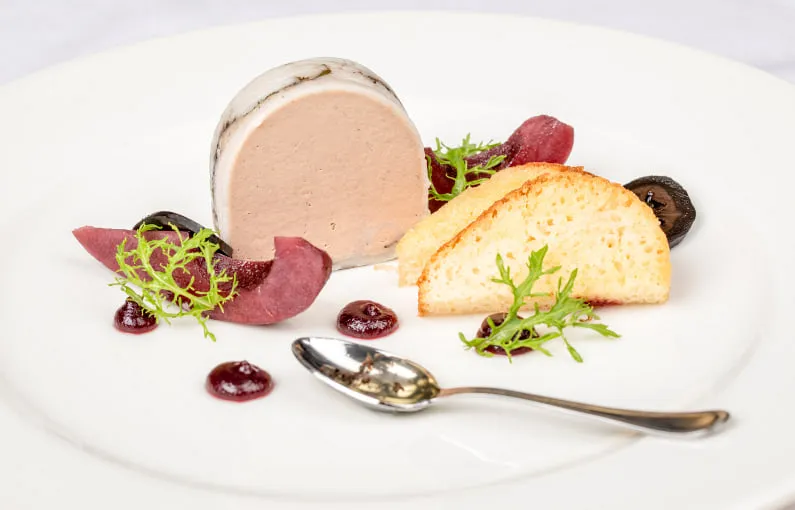 Gourmetgericht mit Terrine, Sauce und Brot auf weißem Teller