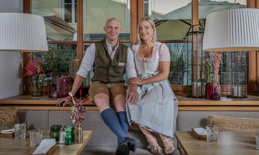 Zwei Personen sitzen in einem Restaurant, gekleidet in traditioneller Kleidung, mit Dekor im Hintergrund.