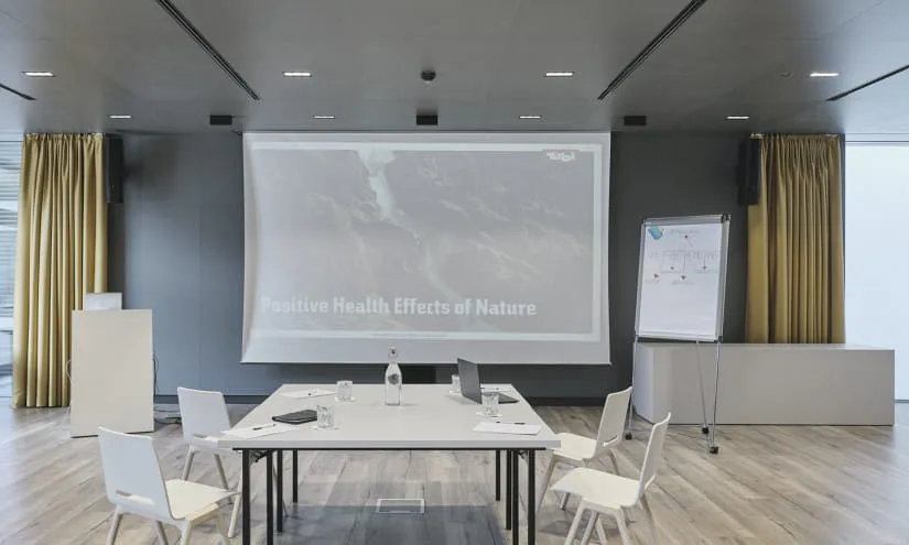 Moderne Konferenzraum mit Tischen, Stühlen und Projektionsleinwand.