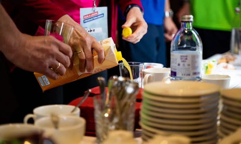 Hände gießen Saft an einem Tisch mit Tassen und Tellern