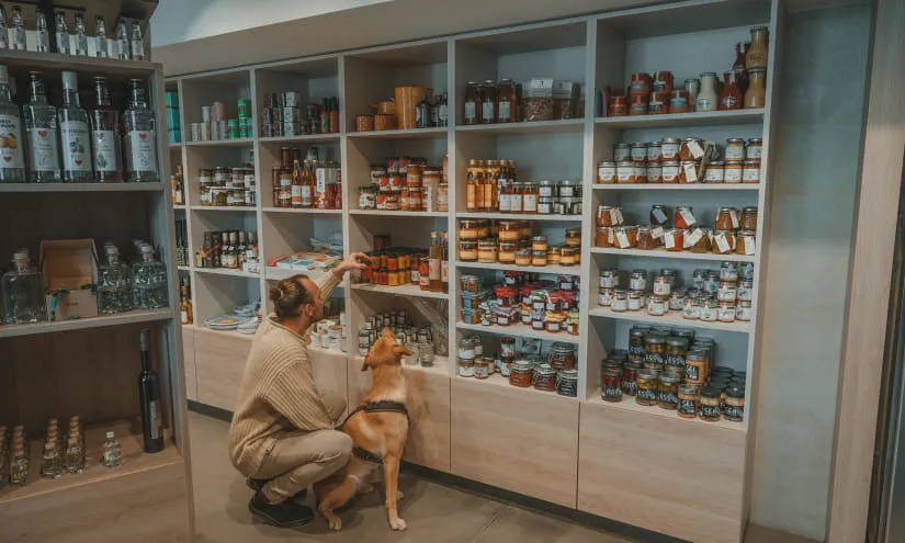 Frau mit Hund vor Regalen voller Konservengläser in einem Geschäft